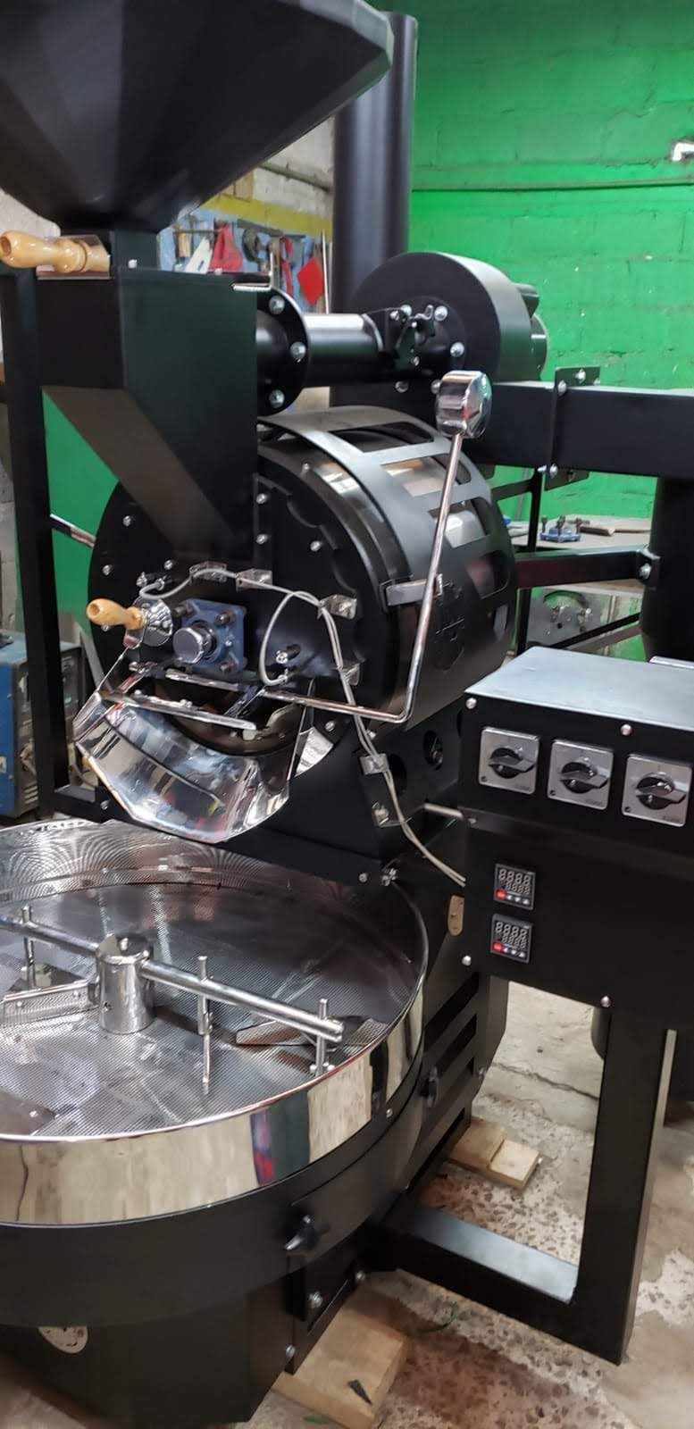 Una imagen de una máquina industrial de tostado de café en funcionamiento. La máquina es grande y tiene un exterior de acero inoxidable. Está tostando granos de café que se están volviendo de color marrón oscuro. La imagen está acompañada de texto que describe los beneficios de usar una máquina industrial de tostado de café.